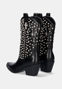 Botas de vaquero de cuero negro con punta afilada, adornadas con tachuelas plateadas y acentos de estrella, con un alto tacón cuadrado y dos tiradores.