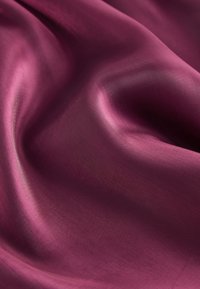 Hedvábná látka v hluboké bordó barvě, s hladkou texturou, mírným leskem a jemným splýváním, zdůrazňující měkké záhyby a křivky.
