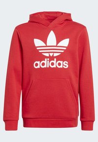 Röd hoodie i bomullsblandning, med en framficka och en stor vit Adidas-logga med tre ränder på bröstet.