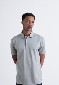 Pilko marškiniai šviesiai pilki, trumpomis rankovėmis, su plokščiu apykakle, trimis mygtukais ir lygiu, tekstūruotu audiniu. Paprastas, universalus dizainas.