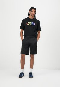Black t-shirt with multicolored "adidas" logo, paired with black striped shorts. Blue athletic shoes and white socks complete the outfit.