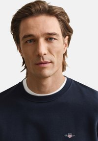 Marineblå crewneck-sweatshirt med ribbede ærmegab og kant, med en lille logo på brystet. Blødt stof med en glat tekstur.