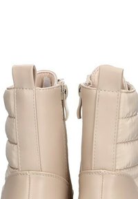 Botas de tobillo beige con textura acolchada, piel sintética suave, cremalleras laterales y tiradores. Diseñadas para facilitar su uso y proporcionar comodidad.