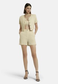 Zweiteiliges Outfit mit einem strukturierten, hellbeigen Crop-Top und passenden hochgeschnittenen Shorts, kombiniert mit einer kurzärmeligen, geknöpften Jacke.