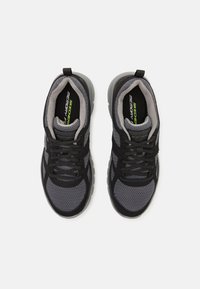 Sapatos de atletismo pretos e cinzas com parte superior em malha, fecho de atacadores, colarinho almofadado e sola flexível; apresenta a marca "Memory Foam" no interior.