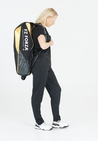 Musta ja kultainen urheilu repull, jossa on pehmustetut hihnat. Varustettu "FZ FORZA" -logolla ja teksturoidulla sivukuviolla. Kantaa olalla henkilö.