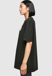 Zwarte oversized T-shirt van katoen, met een grafische print op de voorkant, korte mouwen en een ontspannen pasvorm. Gladde textuur.