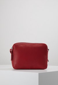 Punainen nahkapussilaukku, jossa on sileä pinta, suorakulmainen muoto, vetoketjusuljenta ja sivulla hapsukoriste. Sopii erilaisille asusteille.