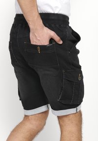 Pantalones cortos de mezclilla negra con un ajuste relajado, que cuentan con un dobladillo enrollado, múltiples bolsillos y detalles de costura en naranja contrastante.