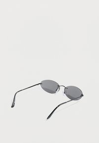 Μαύρα οβάλ γυαλιά ηλίου με σκούρους φακούς, λεπτά μαύρα πλαίσια και διαφανή μαξιλαράκια στη μύτη. Διακοσμημένα με χρυσούς τόνοι στις μεντεσέδες.