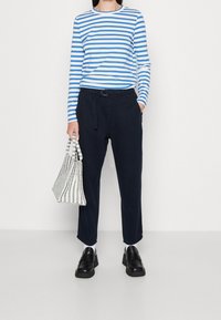 Randig långärmad skjorta i blått och vitt, tillsammans med mörkblå byxor. Svarta slip-on skor och en vävd svart-vit randig väska.