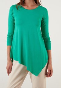 Grön långärmad tröja med rundad halsringning och asymmetrisk fåll. Tillverkad av mjukt material med en slät textur för komfort.