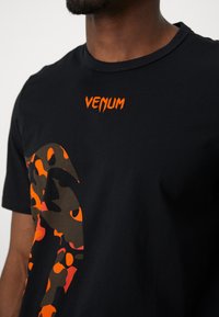 Sort bomulds t-shirt med et stort orange og brunt leopardprint design samt 'VENUM' logo i lys orange på brystet.
