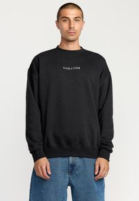 Black sweatshirt with a crew neckline, oversized fit, ribbed cuffs, and a small white "VOLCOM" logo centered on the chest.