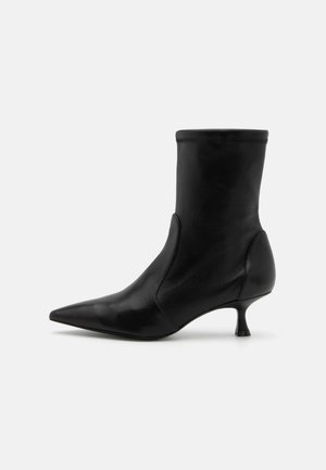 Must musta ankle'iga saabas, millel on kitsenev siluett, elastne ülemine osa ja lühike, õhuke konts. Sile tekstuur ja minimaalne õmblemise detail.