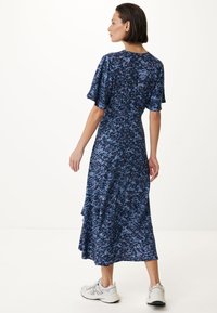 Modrá midi šaty s květinovým vzorem, krátkými volánovými rukávy, vrstvenou sukní a přiléhavým pasem, doplněné bílými sportovními botami.