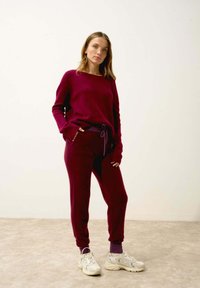Burgundowa sweter dzianinowy z długimi rękawami i luźnym krojem, w połączeniu ze spodniami dresowymi w tym samym kolorze z elastycznym pasem. Uzupełnione szarymi trampkami.