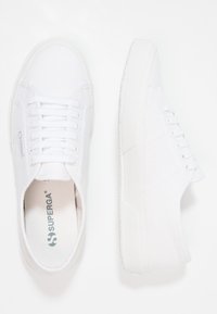 Vita canvas sneakers med en texturerad gummisula, rund tå och platta snören. Har en liten logotyp på sidan och en mjuk innersula.