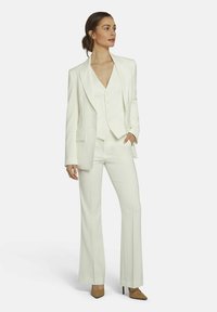 White tailored suit featuring a single-breasted blazer, fitted vest with buttons, and flared trousers. Smooth fabric with subtle sheen.
