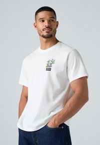 Hvit bomulls t-skjorte med et fargerikt kaktusmotiv og "Levi's"-logo. T-skjorten har rund hals og korte ermer.