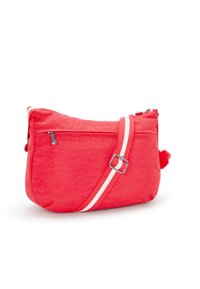 Röd tyg crossbody-väska med dragkedja upptill, vitrandig axelrem och en pom-pom-accent på ena sidan. Slät textur.
