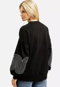 Czarna bluza z długim rękawem, z białym wzorem fali na mankietach. Wykonana z miękkiego materiału, o luźnym kroju i prążkowanym ściągaczu.