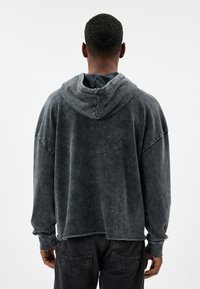 Felpa grigia oversize con texture morbida, caratterizzata da un cappuccio con cordoncino e spalle scese. Il tessuto ha un aspetto vintage sbiadito.