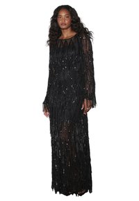 Robe de soirée noire avec un design à franges, recouverte de sequins. Présente des manches longues et une silhouette ajustée, avec des accents en tulle transparent au bas.