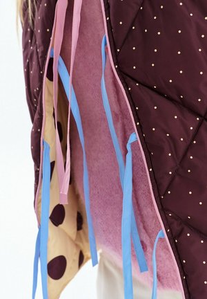 Prešívaná látka so zlatými bodkami, ružová podšívka, béžová látka s veľkými hnedými škvrnami a modré a ružové závesné popruhy alebo šnúrky.
