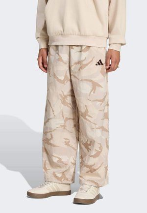 Person trägt creme- und beige Tarnfarbene weite Hose, passenden Pullover und off-white Sneaker mit braunen Sohlen.