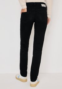 Jeans in denim nero con una vestibilità slim, caratterizzati da due tasche posteriori e una superficie liscia. Indossati con sneakers bianche rifinite con dettagli azzurri.