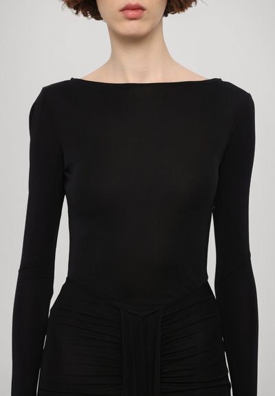 Top negro de manga larga con escote barco. Tela suave con detalle fruncido en la cintura, diseño ajustado y silueta elegante.