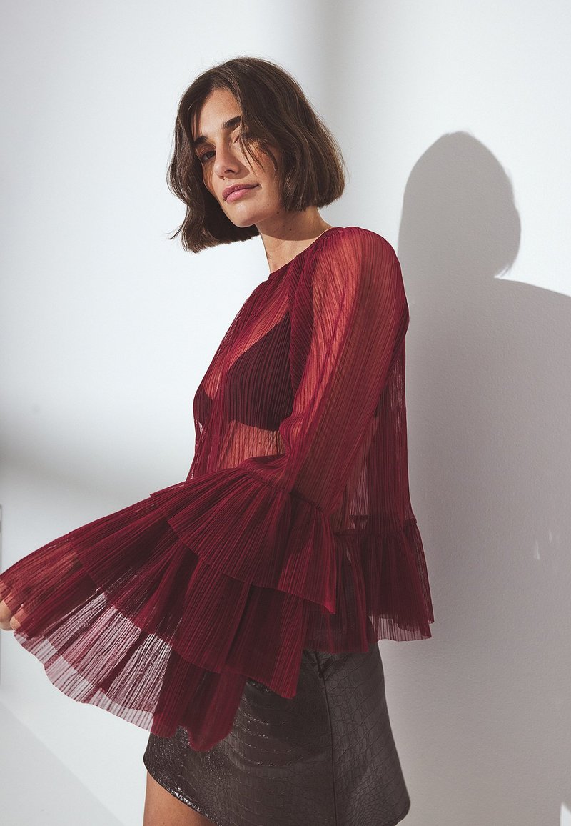Rode geplooide blouse met uitlopende mouwen, semi-transparante stof, gelaagde ruches, gecombineerd met een zwarte textuur rok.