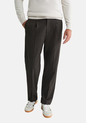 Pantalons plissés gris foncé en tissu texturé, associés à des baskets blanches avec des accents argentés et marron.