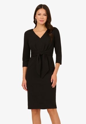 Robe noire à mi-mollet en tissu lisse. Présente un décolleté en V, des manches trois-quarts et un accent de nœud à l'avant au niveau de la taille.