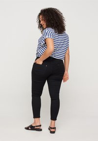T-shirt rayé bleu et blanc associé à un jean skinny noir, avec un design ajusté et des poches arrière. Porté avec des sandales noires.