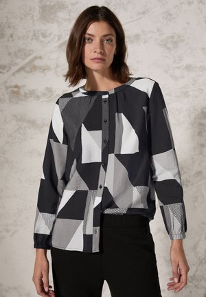 Blouse à motif noir et blanc avec des formes géométriques, devant à boutons, manches longues avec poignets élastiques, fabriquée en tissu léger.