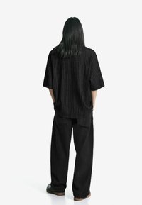 Camicia nera oversize con un motivo testurizzato a coste, abbinata a pantaloni neri dalla vestibilità ampia. L'outfit è completato da calzature nere.