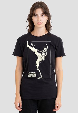 Schwarzes T-Shirt mit kurzen Ärmeln, das ein vintage David Bowie-Motiv in Weiß zeigt, das eine dynamische Pose darstellt, mit Text darunter. Glatte Stofftextur.