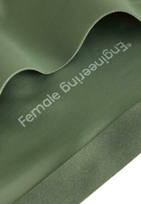 Olivengrønt stof med en glat tekstur, prydet med teksten "Female Engineering" i lysegrå og med en blød foldet kant.