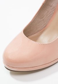 Světle růžová vysoká podpatková bota s lesklým povrchem, zaoblenou špičkou a nízkým předním výstřihem. Vnitřek s texturovaným povrchem a jemnými švy.