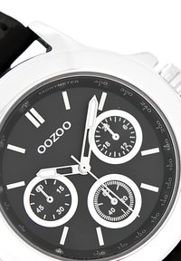 Montre chronographe noire avec des éléments en argent, dotée de trois sous-cadrans, d'index d'heure blancs et d'une échelle tachymétrique sur une lunette brillante.