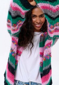 Barevný pletený cardigan s vodorovnými pruhy v růžové, zelené a šedé barvě. Otevřený design a volný střih s texturovaným vzorem příze.
