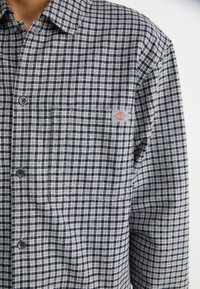 Zwart-wit geblokt overhemd met een kleine rechthoekige Dickies logo patch op de borstzak.