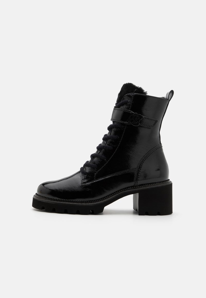 Bottine en cuir noir brillant avec talon bloc, fermeture à lacets à l’avant, doublure en fourrure visible sur le dessus et une sangle latérale avec boucle décorative.