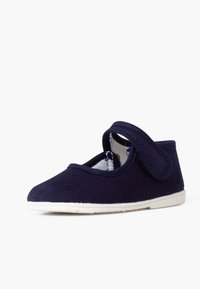 Schuh aus marineblauem Stoff mit einem Klettverschluss, runder Spitze und weißer Gummisohle; das gemusterte Innere ist durch die seitliche Öffnung sichtbar.