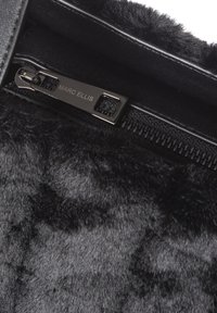 Zwarte imitatiebont binnenkant met een glanzende zwarte ritssluiting voorzien van een merklabel aan het trekkerkoord. Zachte textuur met subtiele kleurvariaties.