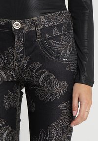 Černé džíny z denimu s podrobným stříbrným listovým vzorem, obsahující texturovanou kapsu s černými flitry a stříbrným knoflíkem.