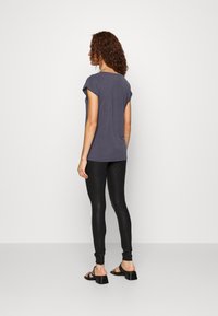 Grå kortärmad skjorta med uppvikta ärmar, kombinerad med svarta leggings med ormskinnsmönster och svarta sandaler med remmar. Enkel och åtsittande design.