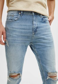 Ljusblå denimjeans med rivna detaljer vid knäna, standard femficksdesign och subtil blekning genom hela tyget.